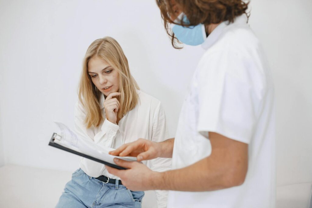 A doctor in a face mask discusses diagnosis with a patient in a clinic setting.