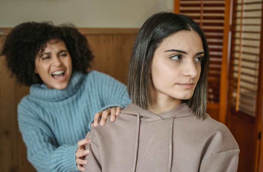 Angry African American female in casual wear screaming and grabbing shoulder of displeased female while having conflict in room at home