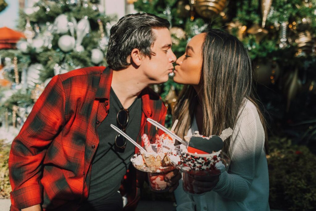 A romantic couple sharing a kiss while enjoying festive ice cream in a decorated outdoor setting.