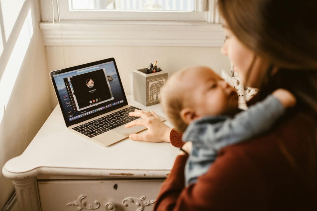 A mother holding her baby while making a video call on a laptop in a cozy home setting.