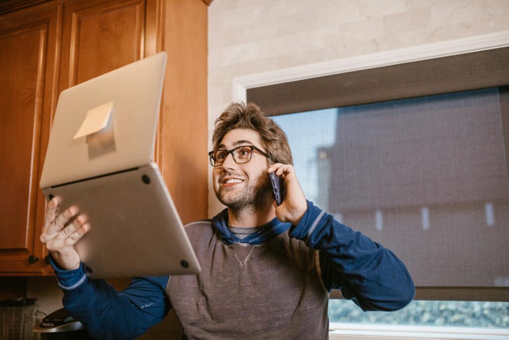 Smiling man multitasking with a laptop and phone for remote online learning.