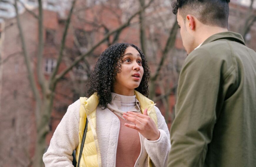 From below of ethnic female with short curly hair standing and arguing with boyfriend on street in daylight