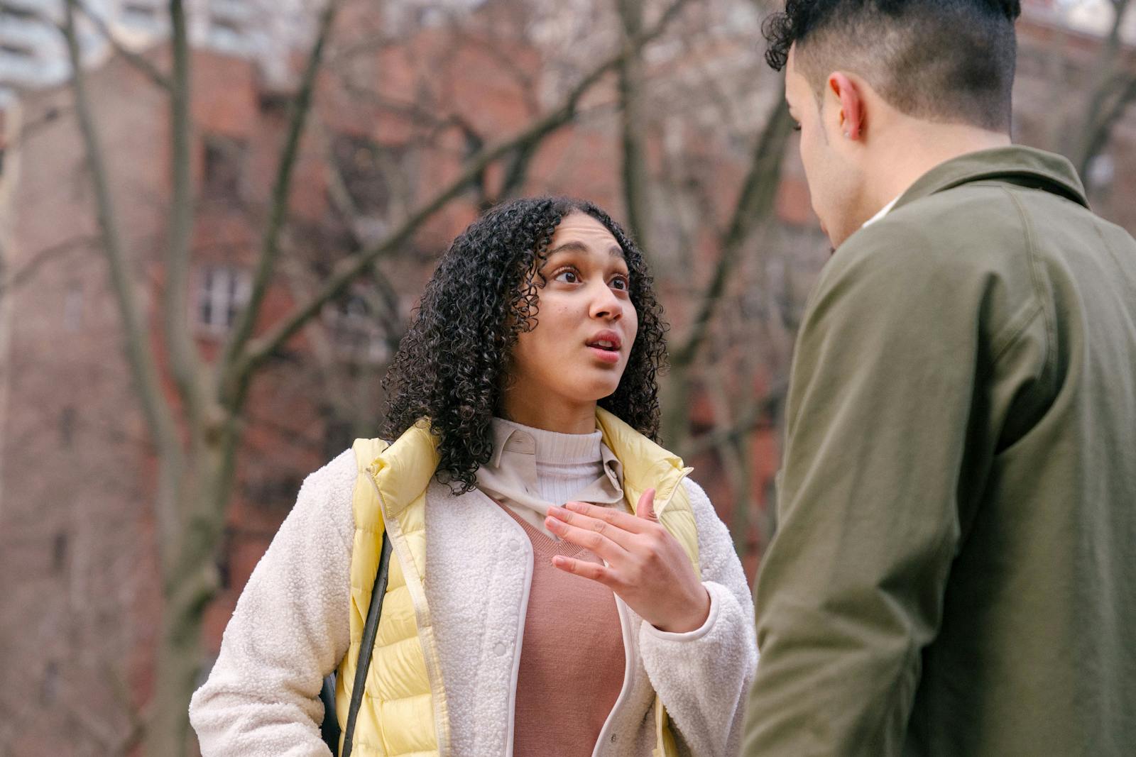 From below of ethnic female with short curly hair standing and arguing with boyfriend on street in daylight