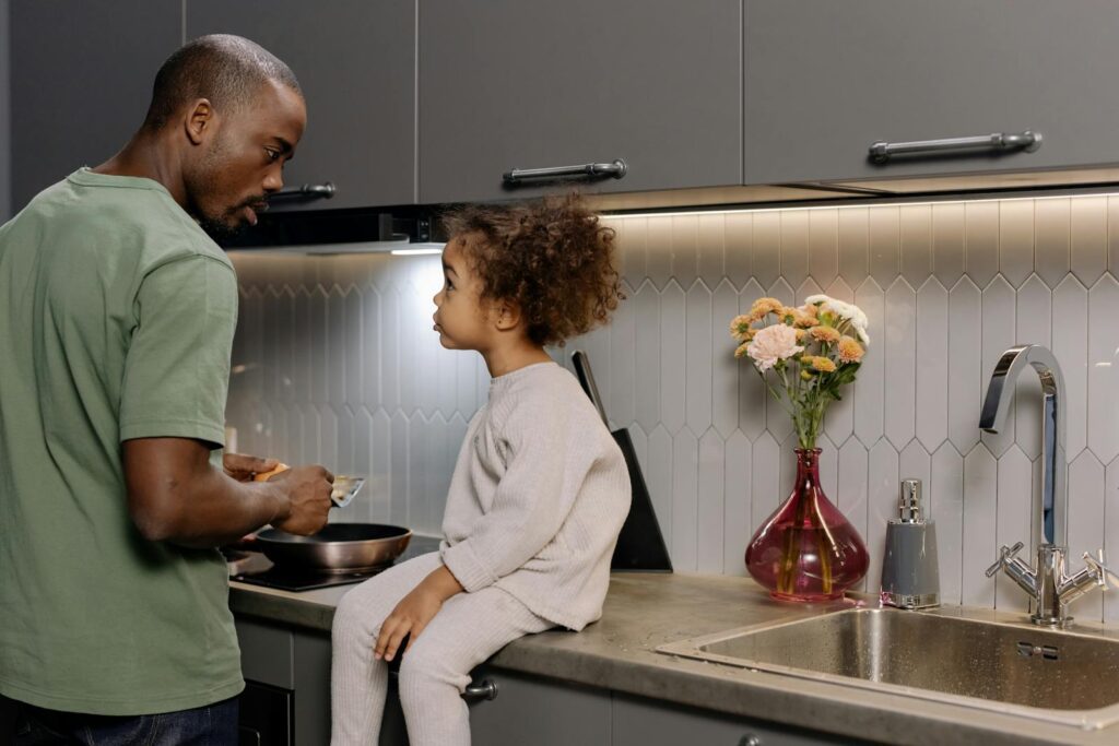 A father and daughter bonding while cooking together in a modern kitchen.