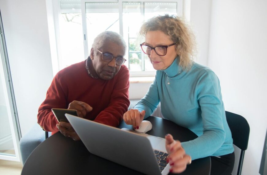 Elderly couple using a laptop in a bright room, focusing on online activities together.