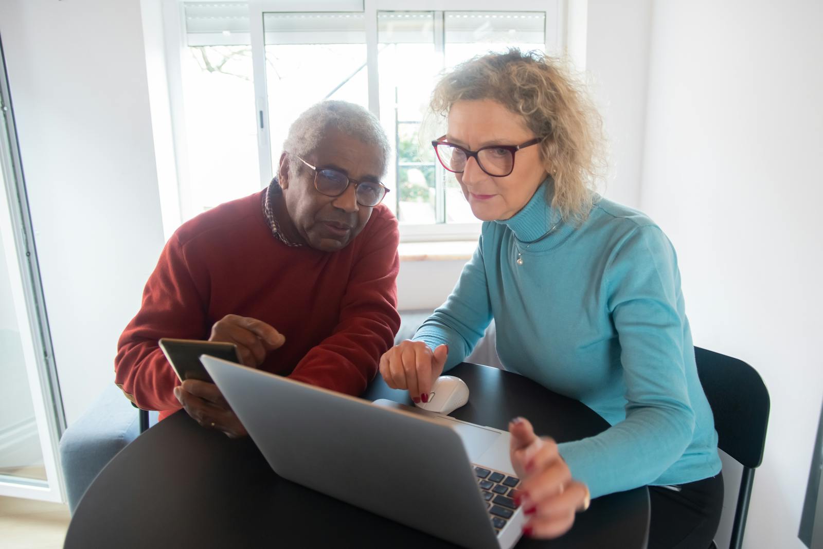 Elderly couple using a laptop in a bright room, focusing on online activities together.