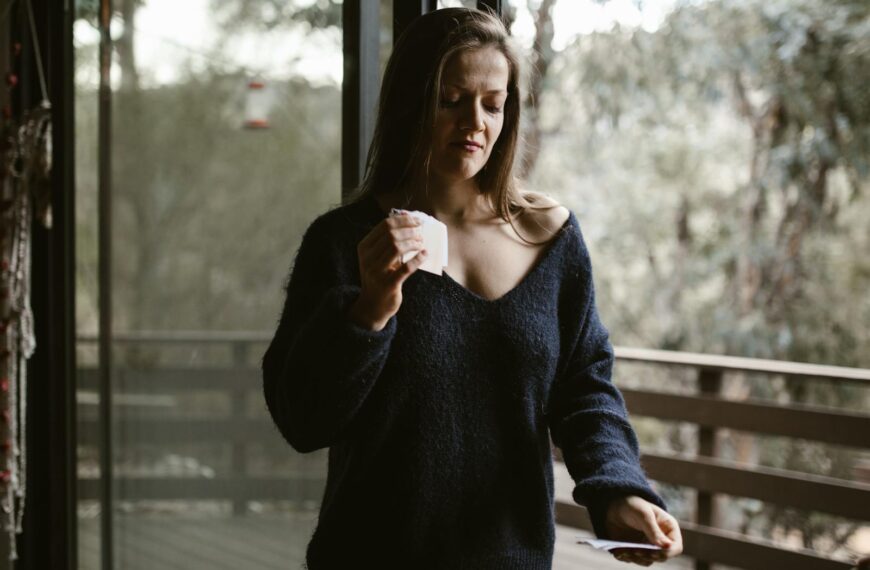 Woman holding papers standing on a balcony, contemplating.