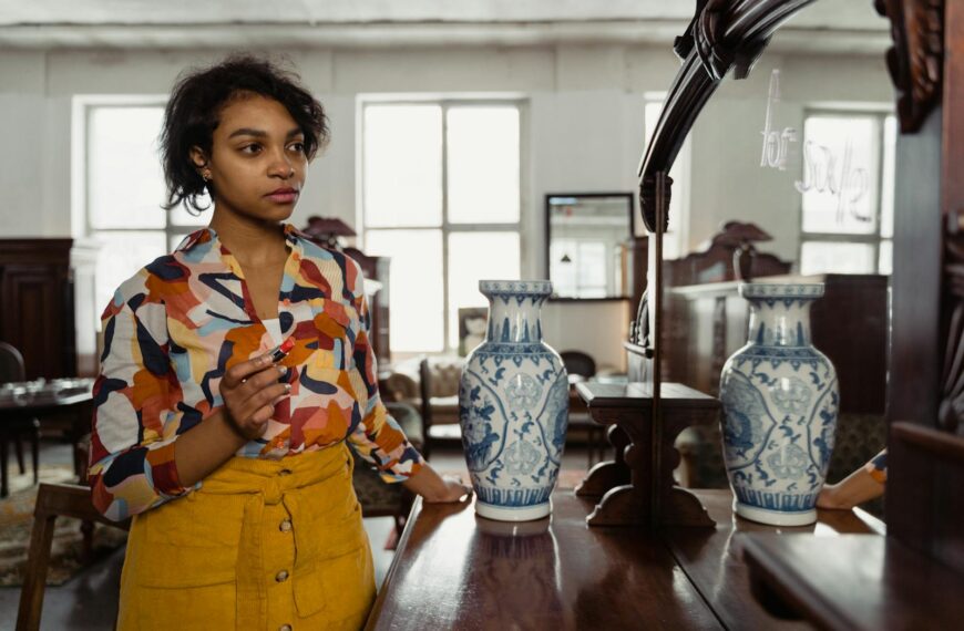 Woman in a colorful shirt admiring her reflection in a mirror with vases, in an antique shop setting.