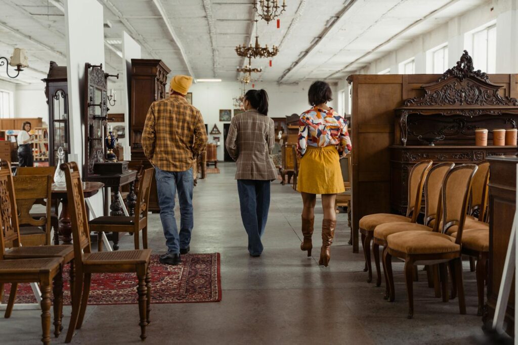 People walking through an antique furniture store, surrounded by vintage chairs and decor.