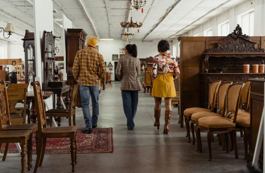 People walking through an antique furniture store, surrounded by vintage chairs and decor.