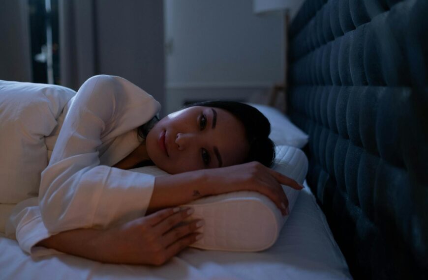 Dark bedroom scene of an Asian woman with insomnia lying on her side, looking thoughtful.