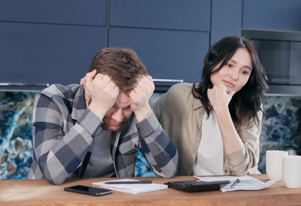 A couple looking worried while reviewing financial documents at a kitchen table.