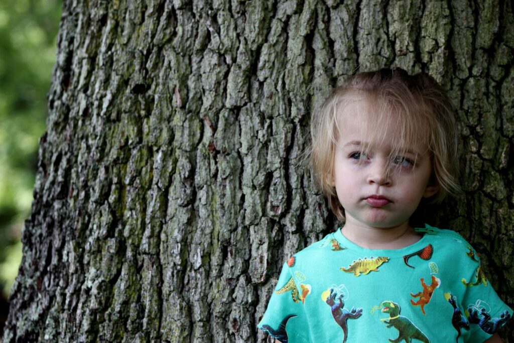 girl wearing multicolored crew-neck shirt laying on brown log bark
