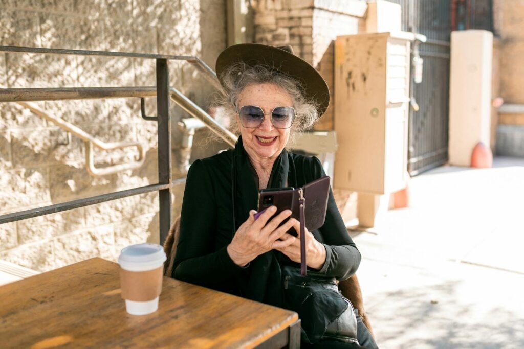 Charming older woman enjoying coffee and using smartphone at an outdoor cafe.