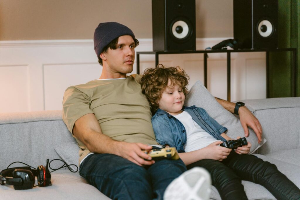 Father and son enjoying a video game session together on a comfy sofa.