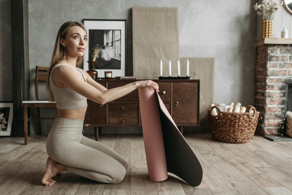 Woman in sportswear rolling a yoga mat in a cozy home interior setting.