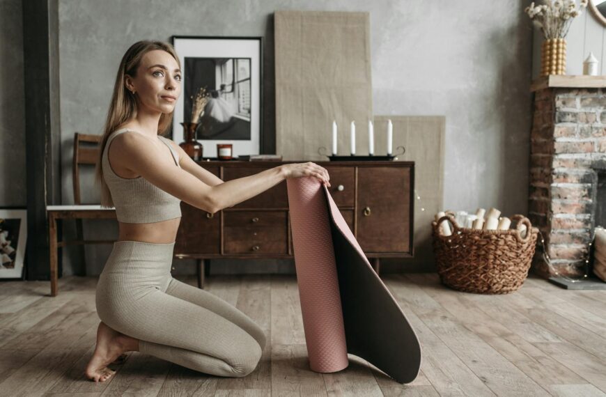Woman in sportswear rolling a yoga mat in a cozy home interior setting.