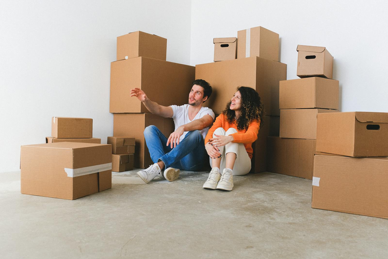 Young couple sitting among cardboard boxes in their new home, taking a break from moving.