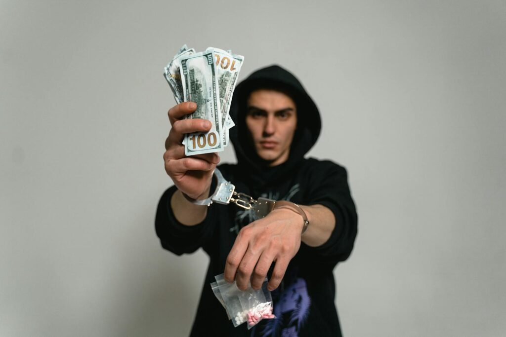Close-up of a man in handcuffs holding cash and drugs, illustrating crime and illegal activities.