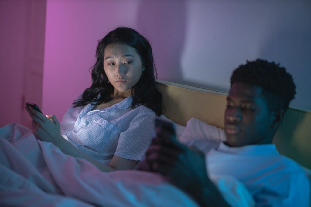 A couple in bed using smartphones, highlighting digital age connectivity or isolation.