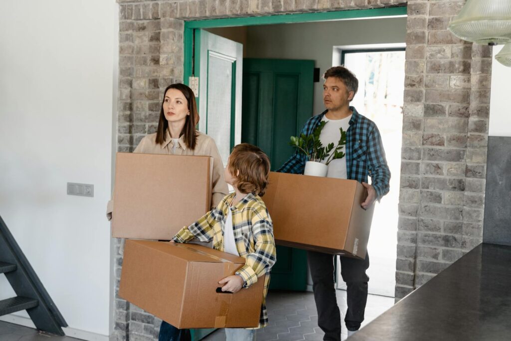 Family entering a new house, carrying boxes and a plant, symbolizing a fresh start.