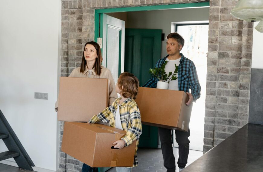 Family entering a new house, carrying boxes and a plant, symbolizing a fresh start.