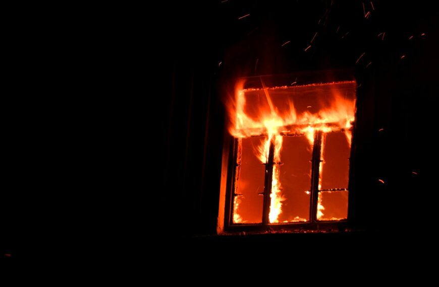 A dramatic scene of a fierce blaze engulfing a window, casting bright flames and sparks against the night sky.