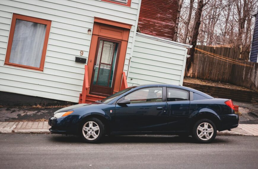 Modern automobile parked on asphalt roadway near aged residential rickety building with window and door located on street of town with leafless trees
