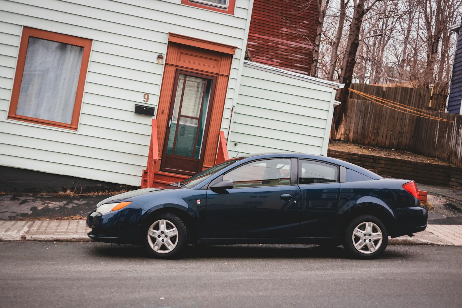 Modern automobile parked on asphalt roadway near aged residential rickety building with window and door located on street of town with leafless trees