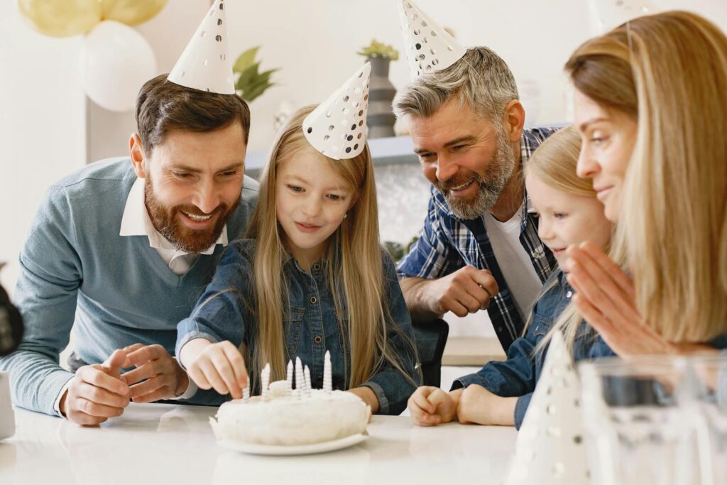 A family enjoys a cheerful indoor birthday celebration with cake and party hats.