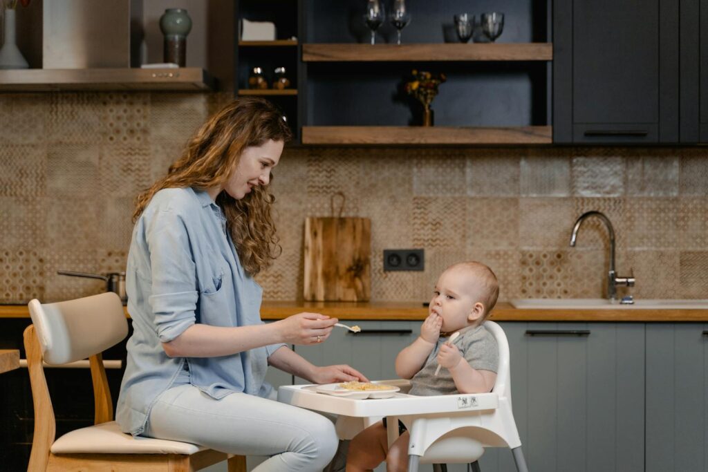 A mother lovingly feeds her baby in a modern kitchen. Heartwarming family moment.