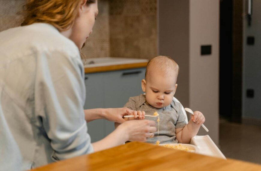 A mother lovingly feeds her baby in a warm and cozy home kitchen setting.