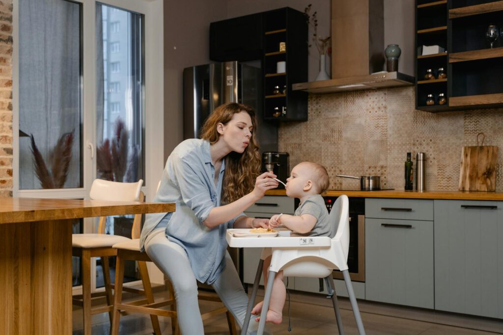 A mother lovingly feeds her baby in a modern kitchen setting.