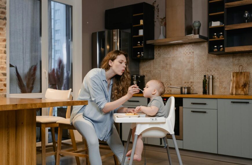 A mother lovingly feeds her baby in a modern kitchen setting.