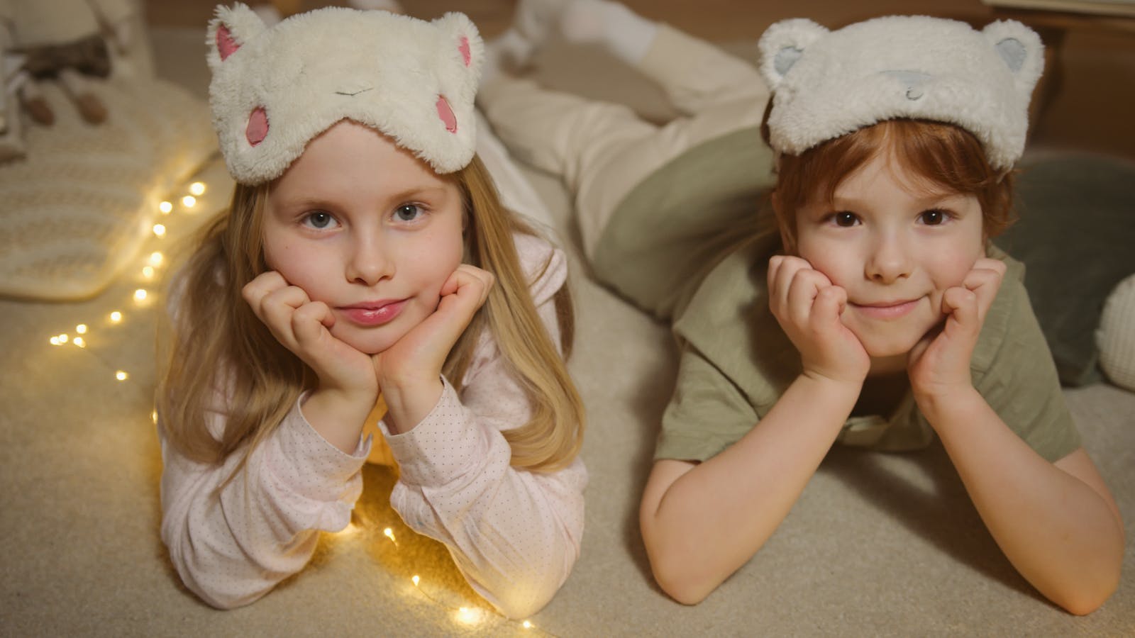 Two children lying on the floor with cute sleep masks, creating a cozy indoor atmosphere.