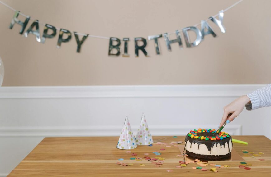 A celebratory birthday cake is sliced, surrounded by party hats and confetti indoors.