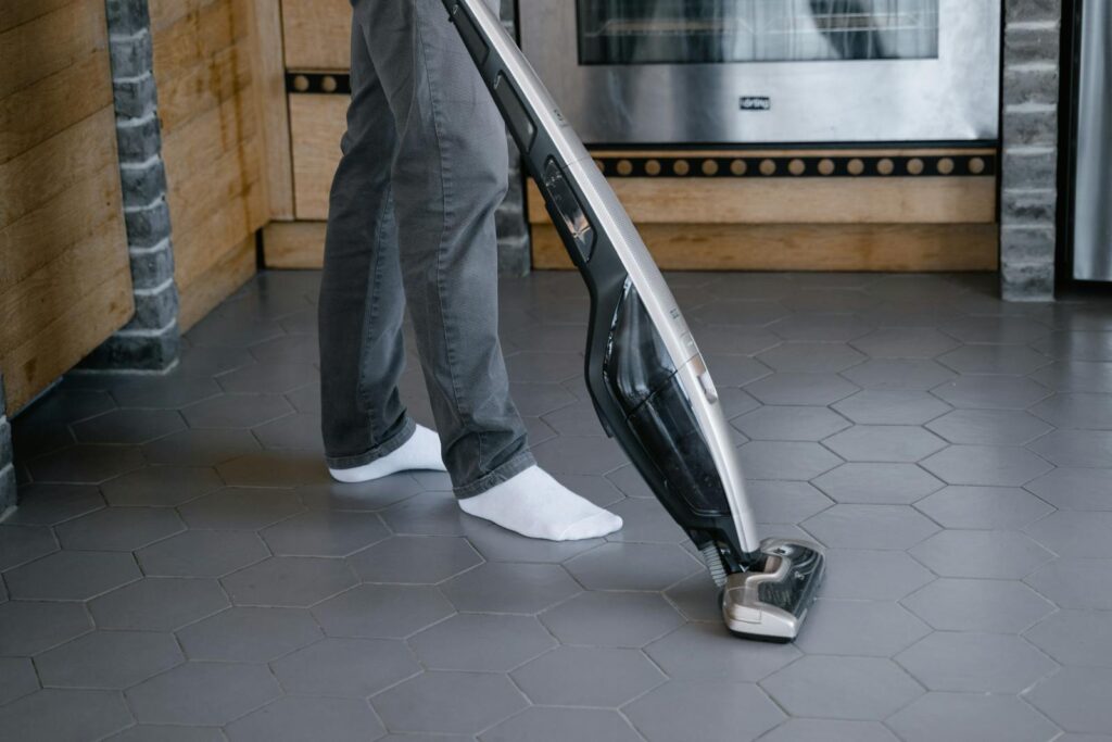 A person cleaning a tiled floor with a modern vacuum cleaner indoors.