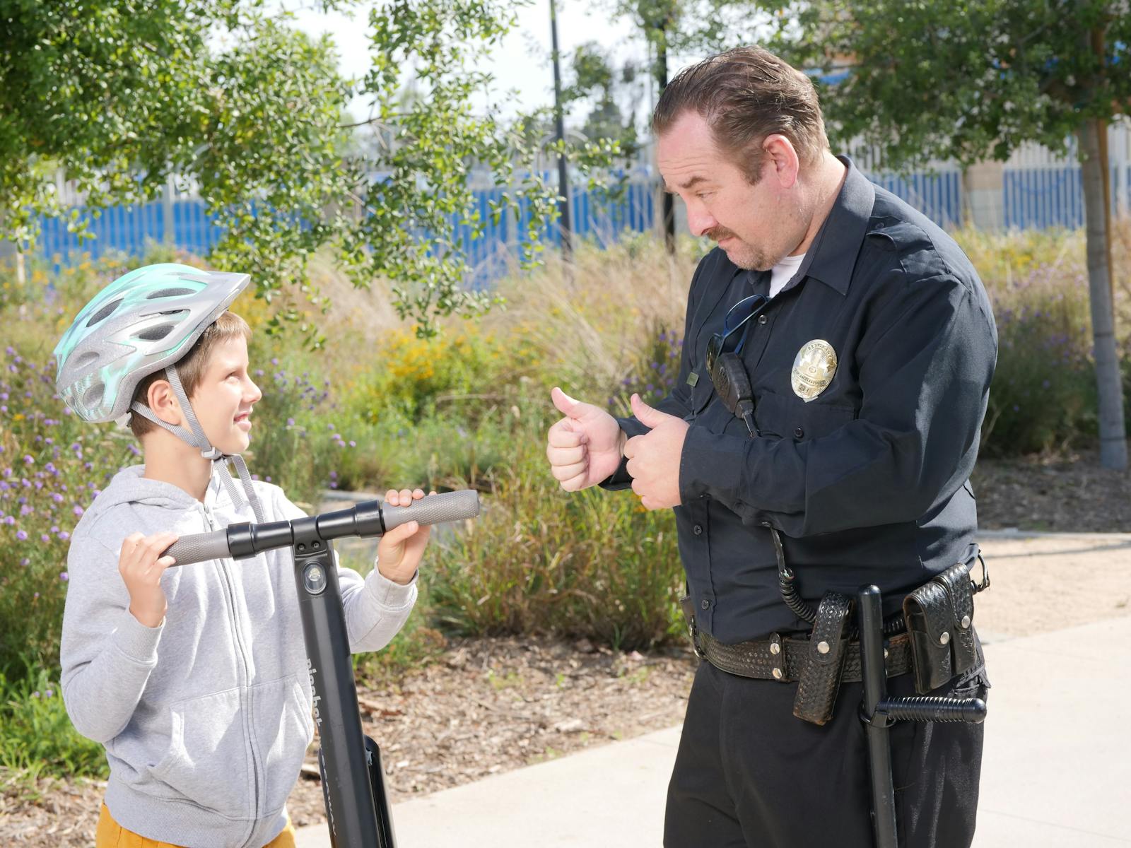 Friendly interaction between a police officer and a child with a scooter, promoting community safety.