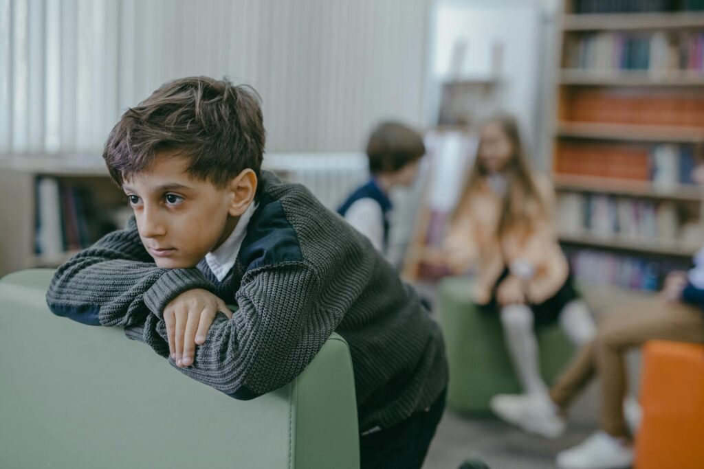 A sad boy leans on a chair in a library, highlighting themes of bullying and loneliness.