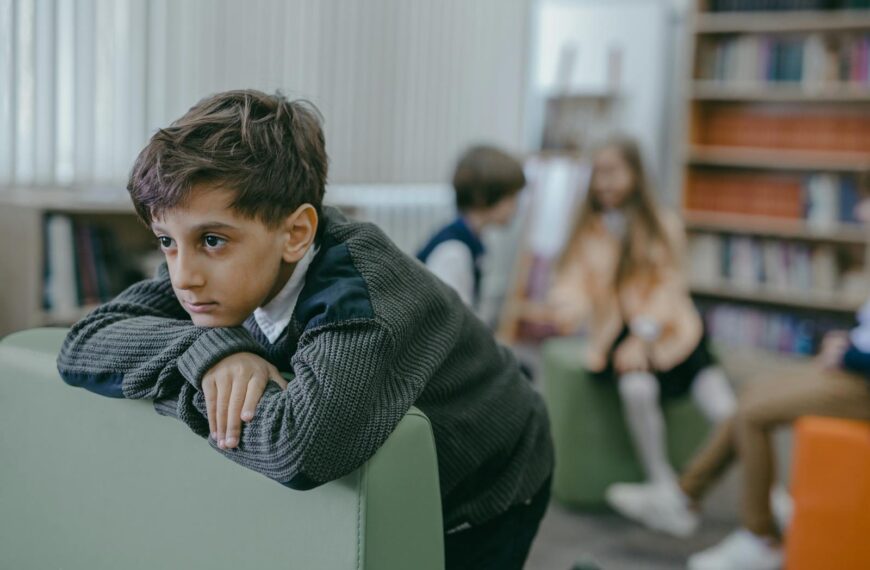 A sad boy leans on a chair in a library, highlighting themes of bullying and loneliness.
