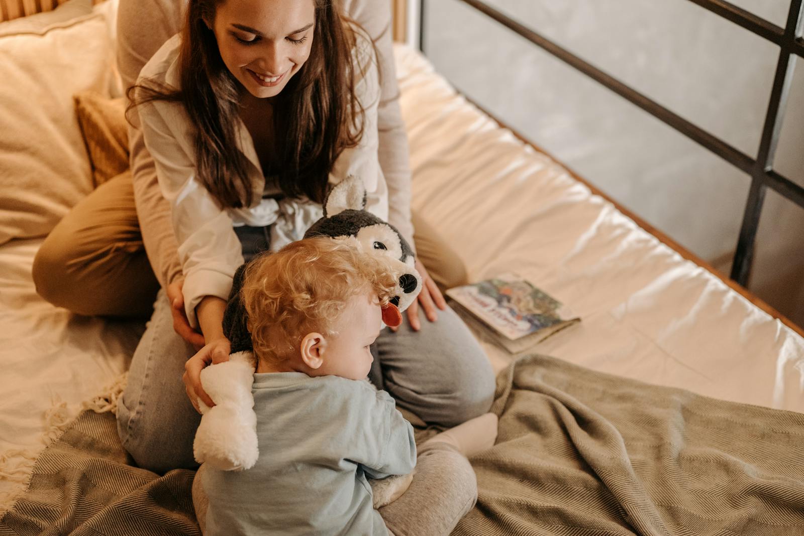 Mother and child bonding playfully on a cozy bed with a toy, capturing affection and happiness.