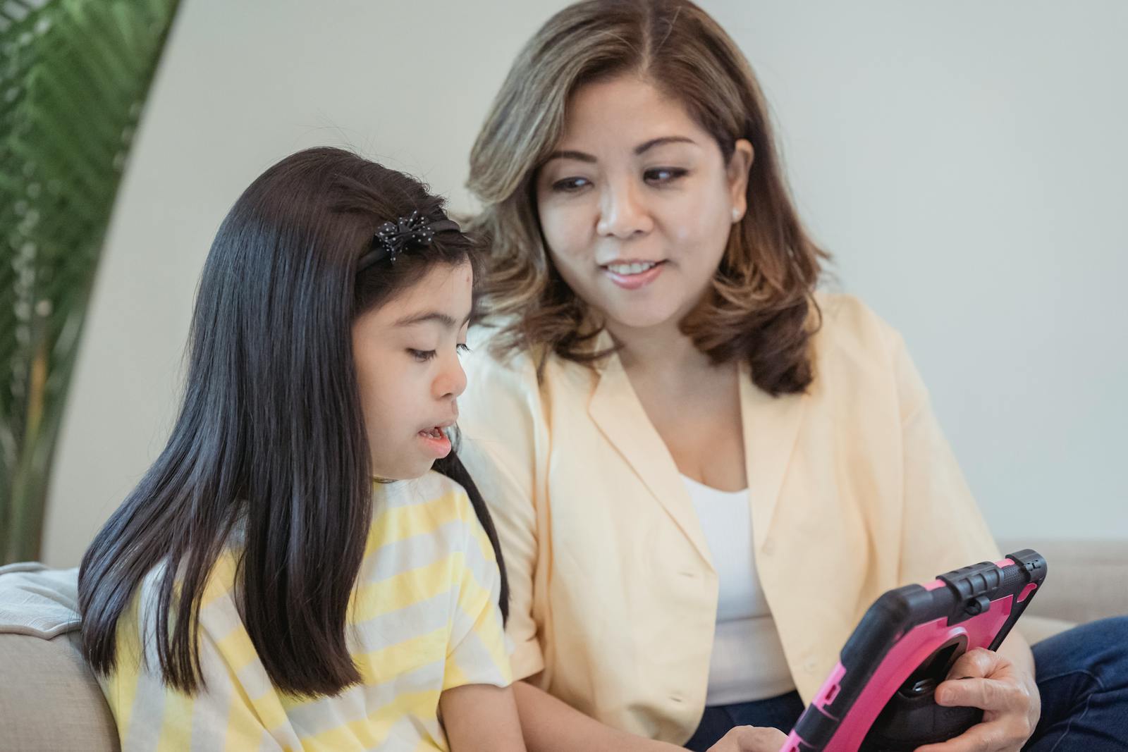 A mother and her daughter bonding while using a digital tablet indoors.