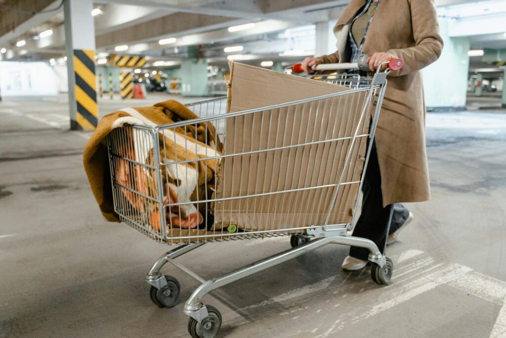 A person pushes a shopping cart with boxes and blankets in a parking garage.