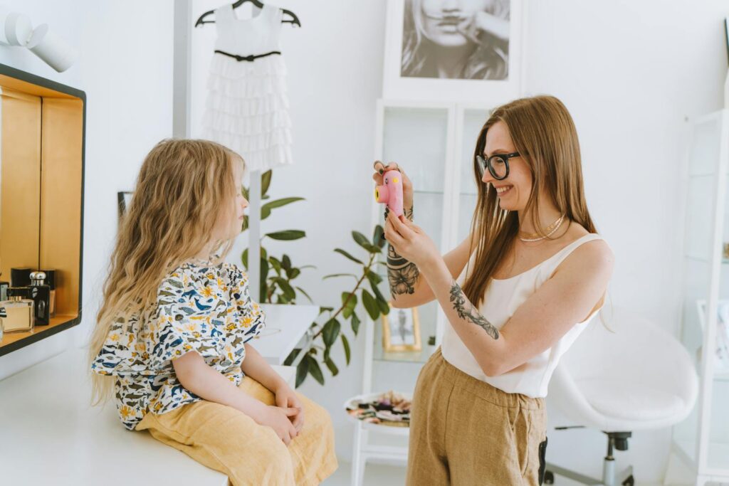 A joyful mother and daughter sharing a moment while taking pictures indoors.