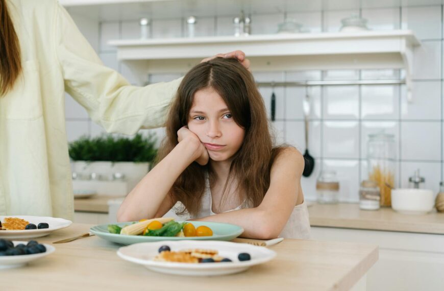 Young girl looking displeased with breakfast in a home kitchen setting.