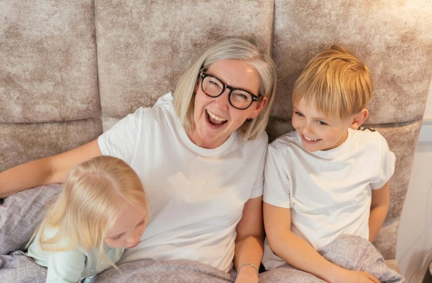 A joyful grandmother with her grandchildren in bed, sharing a happy moment indoors.