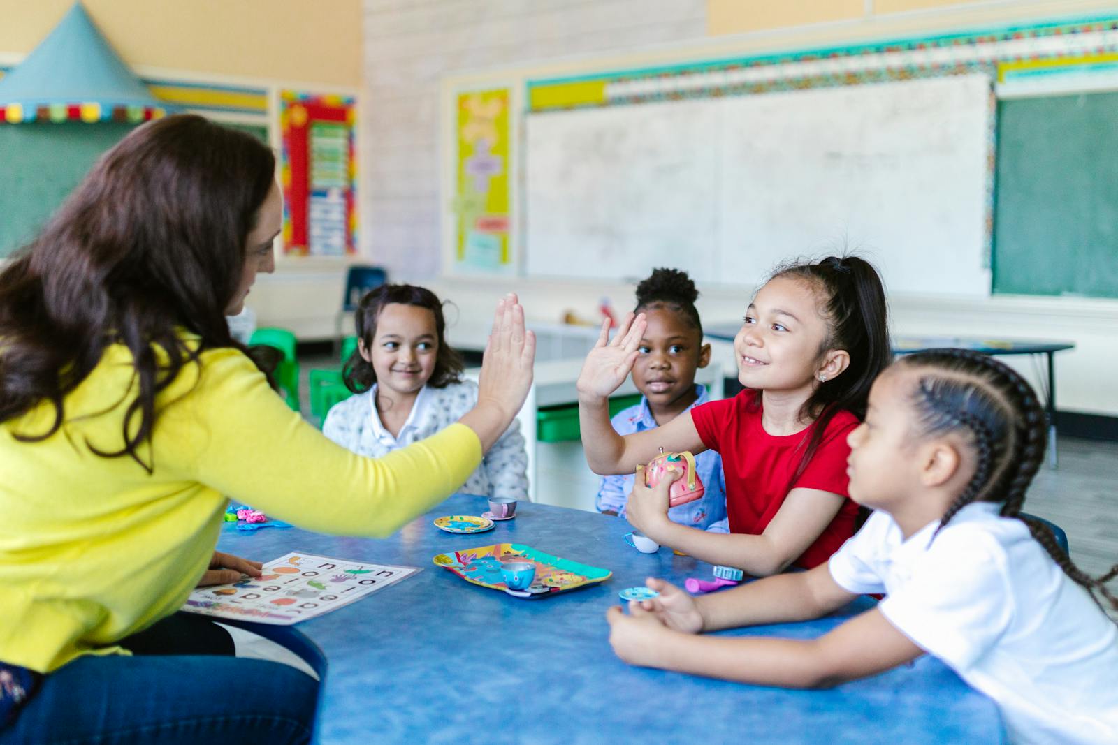 Teacher and diverse students high-five in a lively classroom setting.