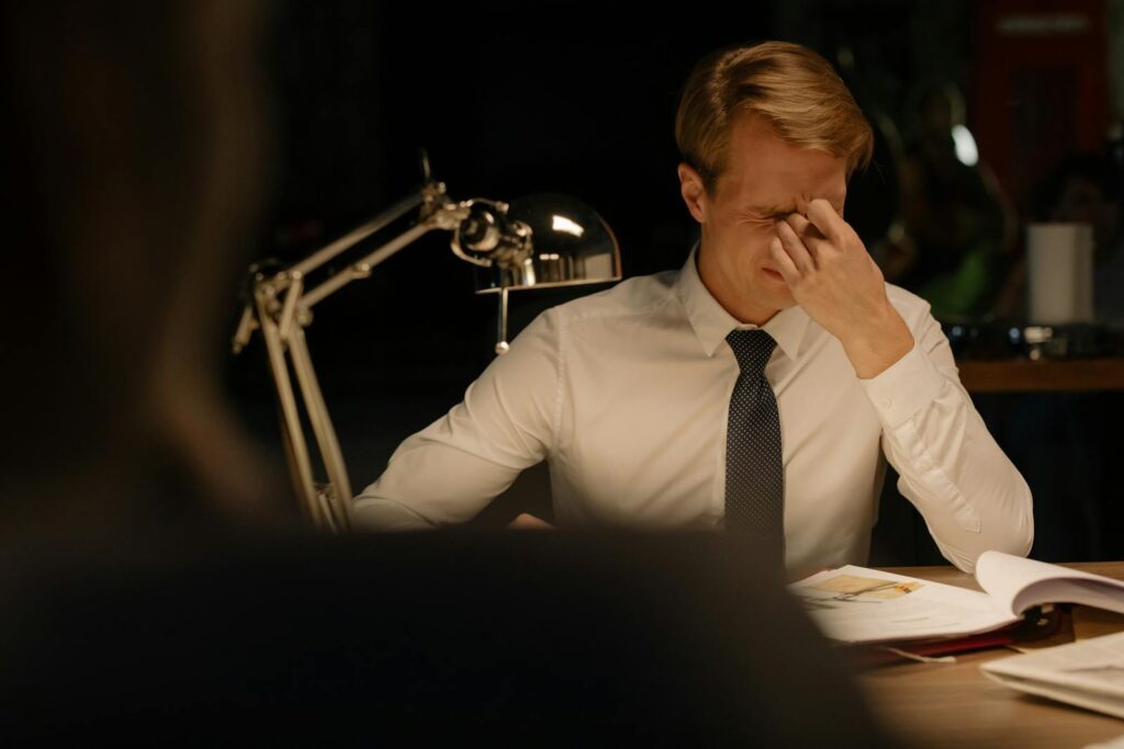 A stressed businessman in a white shirt at his desk, showing frustration.