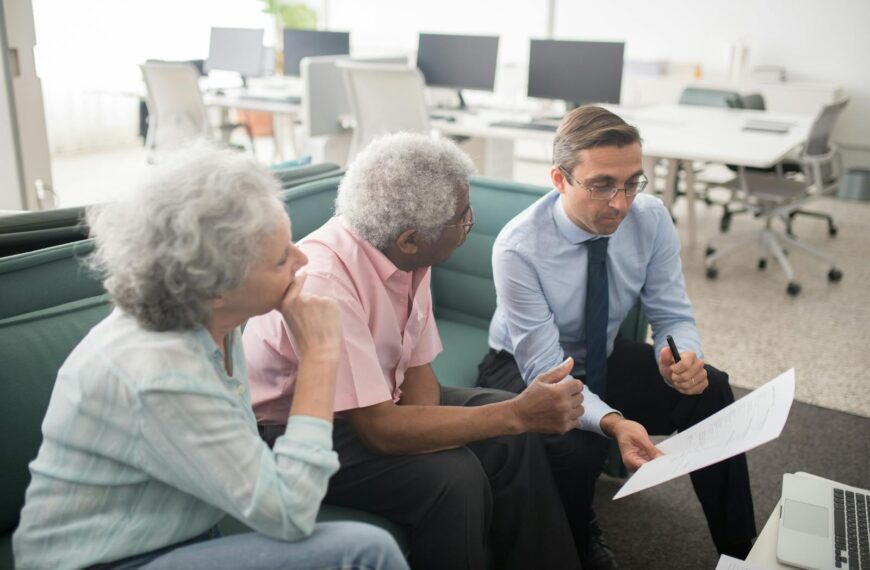 Business professional consults elderly clients in an office setting. Collaborative discussion, paperwork visible.