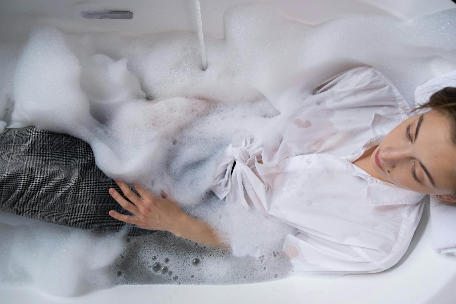 Woman in a bubble bath with white shirt for relaxation and stress relief